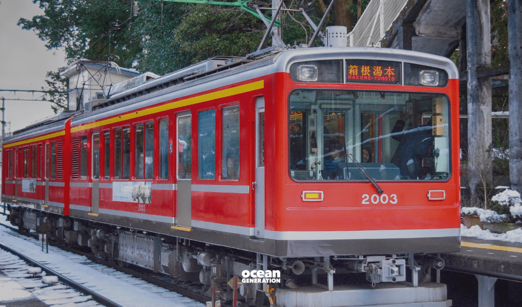 Red train coming to a stop in Japan, shared by Ocean Generation in an article that addresses the environmental impact of how we travel.