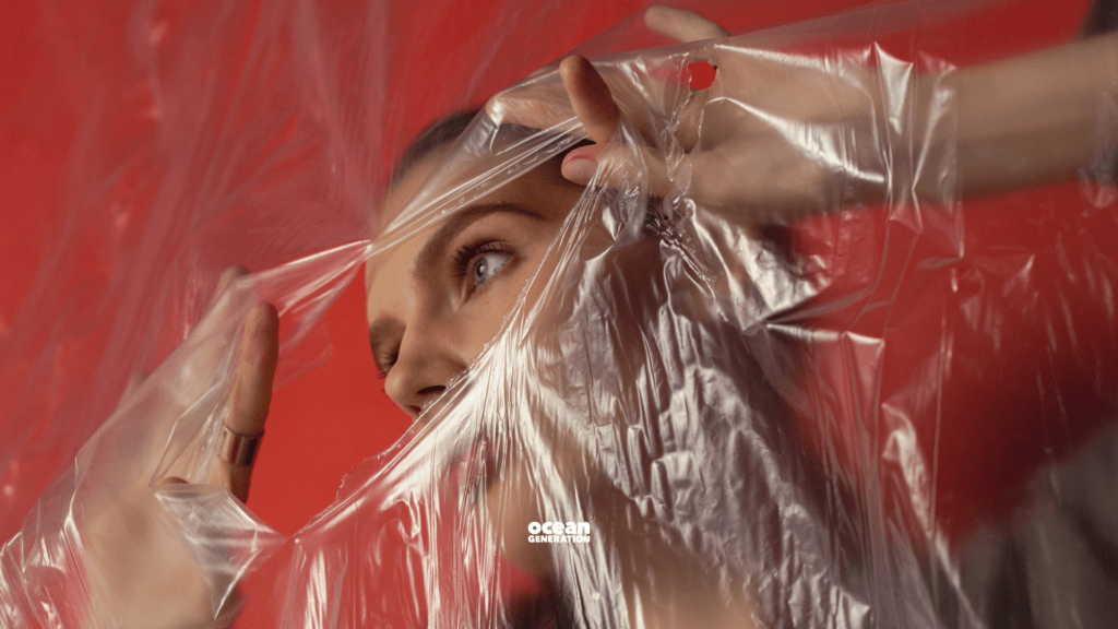 Woman breaking through a piece of clear plastic with her hands. Learn about plastic pollution with Ocean Generation.