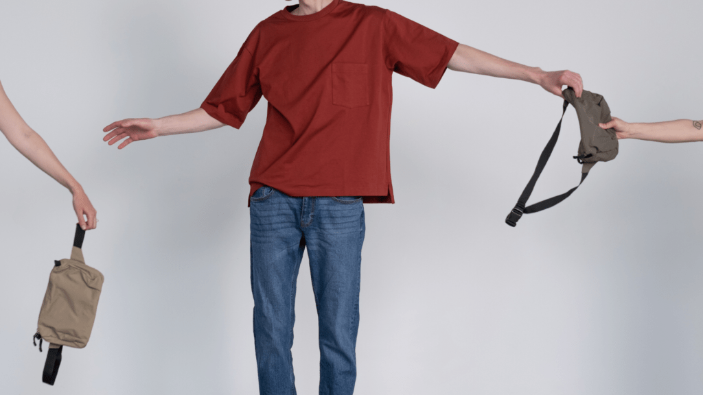 Man in a simple t-shirt and jeans handing off a bag to an extended hand while reaching for a new bag that looks exactly the same. The image symbolises how we over-consume fast fashion. To protect the planet, we need to address our more is best mindset. Ocean Generation is sharing tips to be a more conscious consumer.