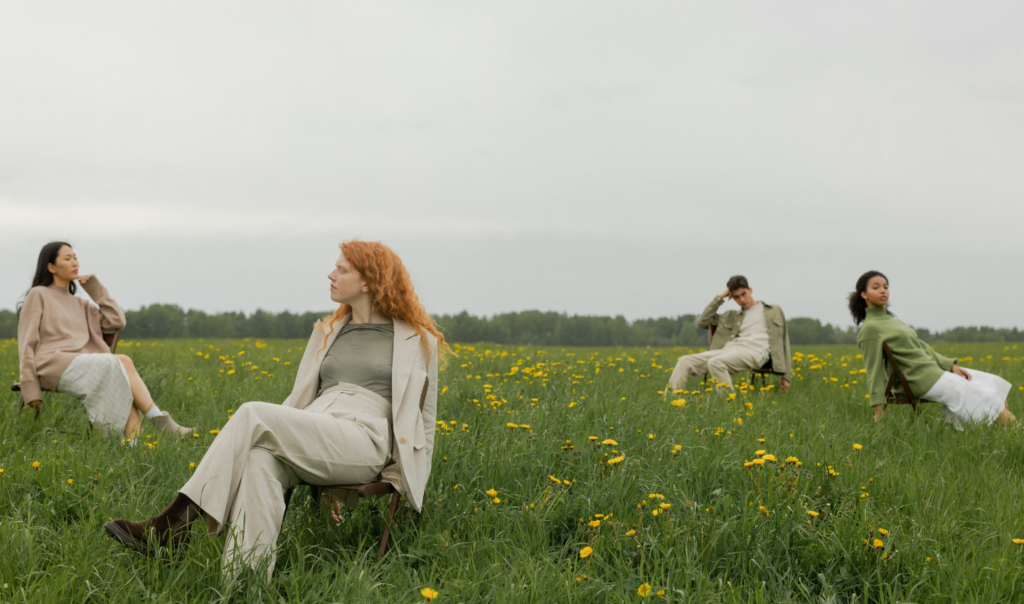 Fashionable women and men sitting on wooden chairs in a lush, healthy field. The people are dressed in sustainable neutrals. In this article, Ocean Generation and Lydia Dupree breakdown what greenwashing is and how to spot it.