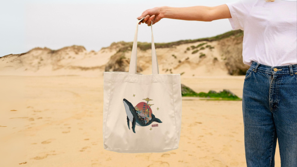Woman on the beach, with an Ocean-friendly beach bag sold by Ocean Generation. Whale beach bag. Ocean Generation's clothing products are all sustainable, using organic cotton and 100% renewable energy to manufacture the items.